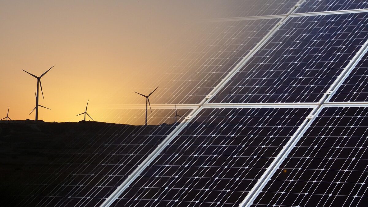 Panneaux solaires au premier plan et éoliennes à l'arrière-plan sur une colline, au coucher du soleil.